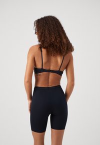 Svart åtsittande sport-bh med justerbara axelremmar, kombinerad med högmidjade svarta cykelshorts. Slät tygkvalitet, minimalistisk design utan dekorationer.