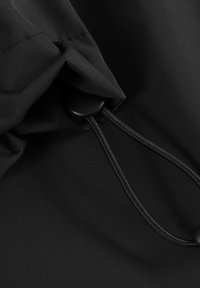 Tela negra con un cordón ajustable y un tope de plástico utilizado para apretar o ajustar la ropa o las bolsas.