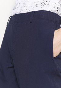 Námořnické kalhoty s hladkou texturou, které mají boční kapsy a přiléhavý pas. Tkanina se zdá být lehká s jemnými detaily šití.