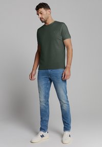 Korte mouwen donker groene T-shirt met een klein logo, gecombineerd met lichtblauwe jeans en witte sneakers. Gladde stofstructuur, casual pasvorm.