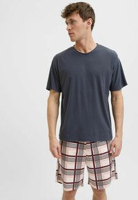 Ciemnoszary t-shirt z krótkim rękawem w połączeniu z jasnoróżowymi szortami, które mają wyrazisty bordowy i czarny wzór w kratkę, gładką fakturę i luźny krój.