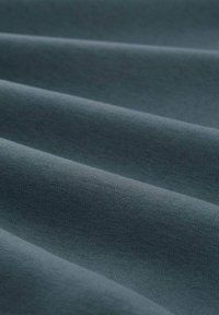 Pehme materjal sügavas smaragdrohelises värvitoonis, millel on sile tekstuur, sisaldades peent voldimist ja ühtlast kudumismustrit kogu ulatuses.