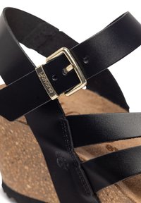 Sandal in pelle nera con tre cinghie, un accento in fibbia dorata e una suola in sughero a zeppa con superficie testurizzata.