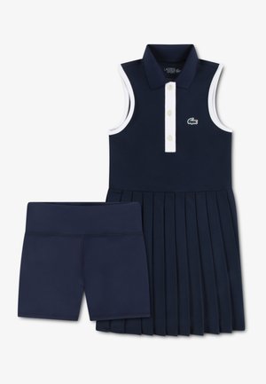 Robe polo sans manches bleu marine avec accents blancs et jupe plissée, associée à un short bleu marine assorti, avec un petit logo vert en détail.
