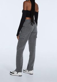 Graue Cargo-Hosen mit Seitentaschen, gerader Schnitt und weicher Textur. Kombiniert mit einem schwarzen Langarmoberteil und weißen Sneakern.