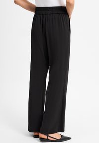 Zwarte wijde broek met een elastische tailleband, voorzien van zijzakken en een gladde, lichtgewicht stof, gecombineerd met zwarte instappers.