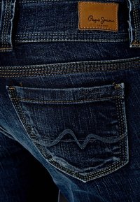 Mörkblå denimjeans med en distinkt design på bakfickan med stickade detaljer. Inkluderar en brunt lädermärke.