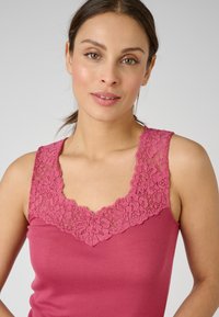 Top senza maniche fucsia con scollatura in pizzo floreale. Il tessuto morbido e elasticizzato e il design aderente mettono in risalto i dettagli intricati in pizzo del colletto.