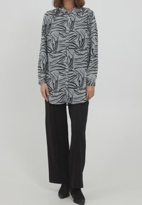 Camisa de botones en blanco y negro, con un patrón de ondas, mangas largas y un cuello con solapa, combinada con pantalones de pierna ancha negros.