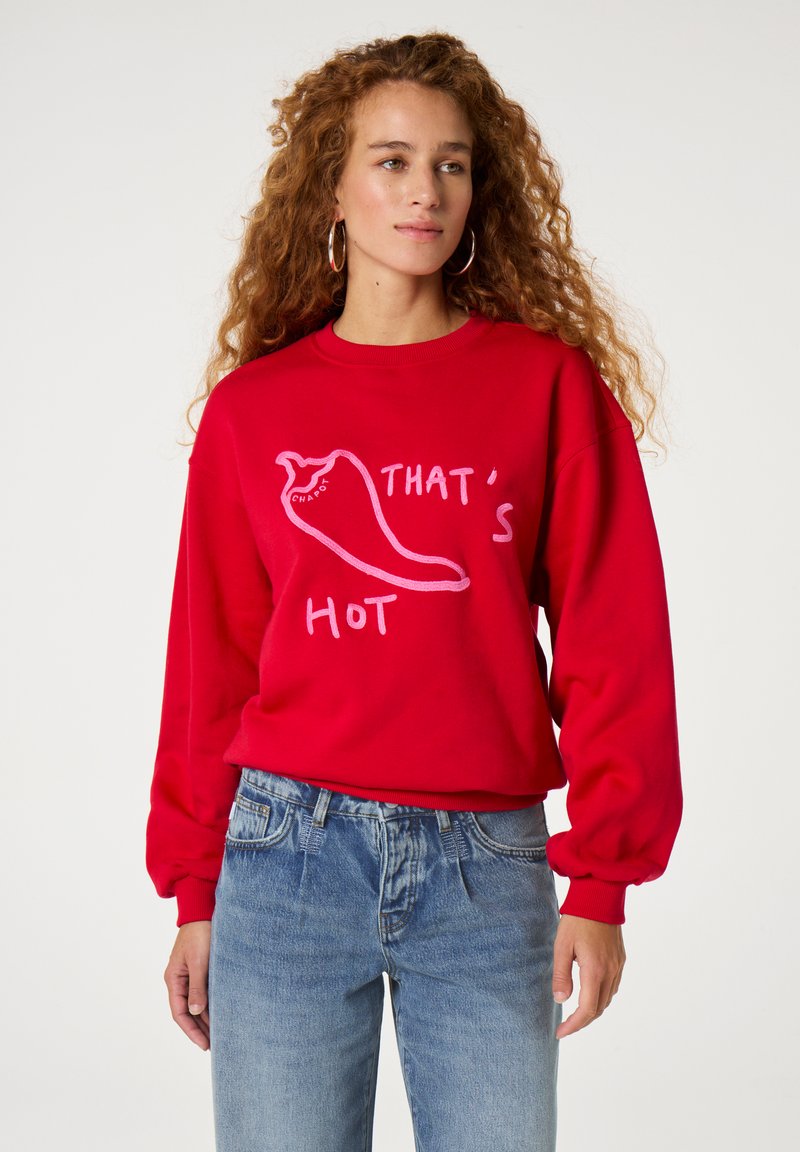 Roter Sweatshirt mit einer Chili-Pfeffer-Grafik und dem Text "DAS IST HEISS" in Pink. Das Design hat eine lässige Passform und gerippte Bündchen.