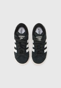 Black suede sneakers featuring three distinctive white stripes, lace-up design, and a rubber sole with an embossed logo on the tongue.
