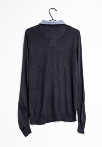 Granatowy sweter z długim rękawem o textured wykończeniu i niebieskim w kratkę kołnierzyku. Posiada prążkowany dół i mankiety, wisi na czarnym haku.