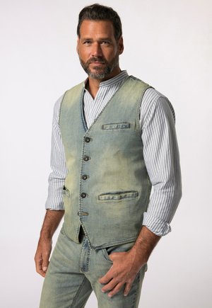 Denimweste in hellblauen und verblasst grünen Farbtönen, mit fünf Knöpfen, zwei Taschen und einem taillierten Schnitt. Trägt sie über einem gestreiften Hemd.