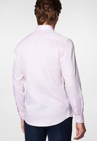 Jasnoróżowa koszula z długim rękawem, wykonana z gładkiego materiału, z guzikami przy mankietach, półokrągłym dołem i klasycznym kołnierzykiem. Tylny widok ukazuje dopasowany krój.