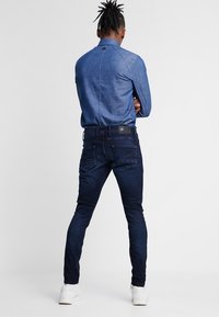 Mörkblå denimjeans med slim fit, med en läderlapp bak, och en ljusblå denimskjorta med en stilren krage.