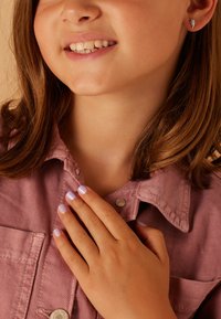 Lila nagellak op een hand die rust op een roze overhemd met kraag. Het oor heeft een klein zilveren oorbel in de vorm van een vleugel. Gladde huidtextuur.