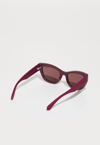 Burgundy napszemüveg szögletes keretekkel, árnyékos lencsékkel és vékony karokkal, amelyeken a Polaroid logó található. Könnyű műanyagból készült.