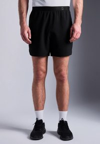 Svarte atletiske shorts med elastisk midje, glatt stoff og ingen synlige mønstre. Brukes med svarte sko og hvite sokker.