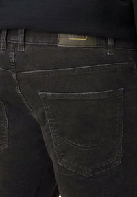 Zwarte corduroy broek met twee achterzakken met ronde naden, een gestructureerde afwerking en een groene leren logo patch nabij de tailleband.