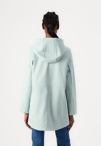 Lys myntegrønn regnjakke med hette, lange ermer og lett avrundet kanten. Har en glatt tekstur og minimalistisk design.