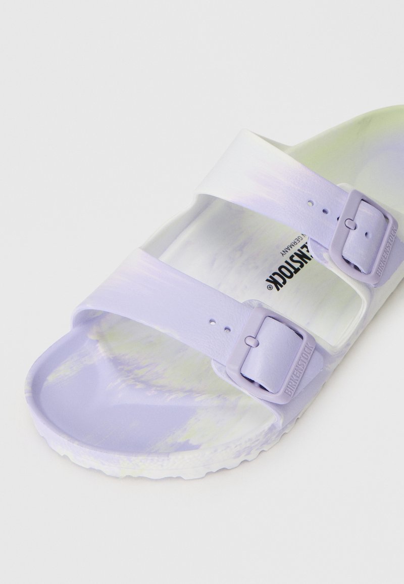 Lila Flip-Flops mit doppelten Riemen aus weichem Material, ausgestattet mit zwei verstellbaren Schnallen und einer strukturierten Sohle mit einem marmorierten Muster auf dem Fußbett.