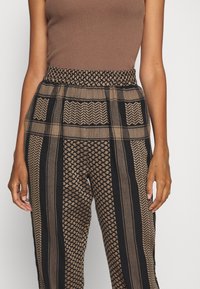 Mönstrade byxor med en blandning av fiskbensmönster och geometriska designer i brunt, svart och tan, med ett elastiskt midjeband för komfort.