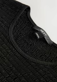 Haut noir présentant un design texturé et froncé, avec un col rond et une finition en tissu lisse. L'étiquette au niveau du col indique "NEXT".