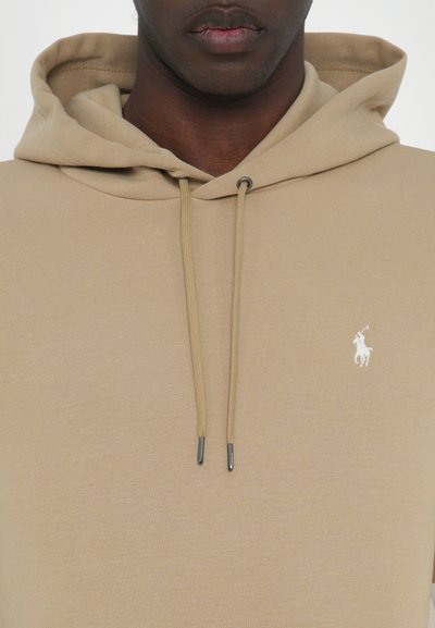 Tan hoodie made of smooth fabric featuring a kangaroo pocket, drawstrings with metal tips, and a small white logo on the chest.