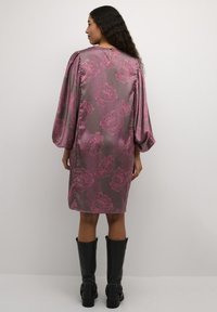 Satinklänning i mauve med rosa blommönster, med puffärmar och en nyckelhålsdetalj bak, kombinerad med knähöga svarta stövlar.