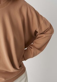 Felpa marrone, morbido misto cotone, vestibilità rilassata, colletto e polsini a costine, con cuciture laterali e orlo leggermente curvato.