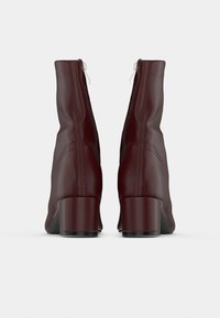 Paire de bottines en cuir rouge foncé avec talons carrés, vues de dos sur un fond blanc uni.