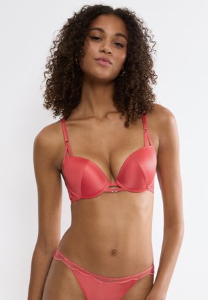 Coral push-up bra with smooth fabric, underwire support, adjustable straps, and a decorative front clasp detail. Matching sheer thong.