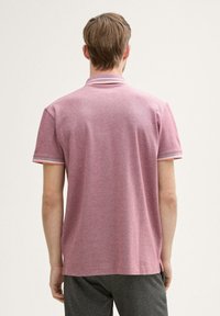 Rød polo-shirt med tekstureret overflade, med en klassisk krave og kontraststribede detaljer på ærmerne og kraven.