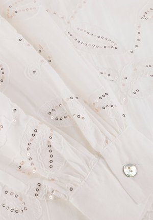 Witte stof met geborduurde bloemenpatronen. Voorzien van pailletten in roségoud en zwart. Manchetknopen hebben een geplooide textuur en een glanzend knopdetail.