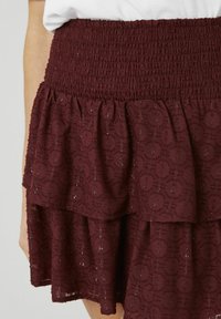 Jupe à volants couleur bordeaux avec une ceinture smockée, présentant un motif texturé et un léger éclat sur l'ensemble du tissu.