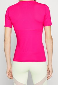 Tajt, kortärmad topp i klar rosa, tillverkad av flexibelt tyg med en slät yta. Har en enkel rund halsringning och minimal varumärkesprofil.