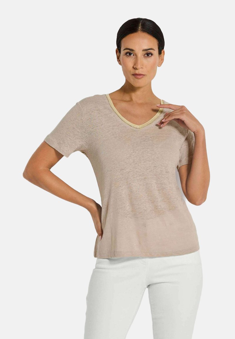 Beige Kurzarm-T-Shirt mit V-Ausschnitt und kontrastierendem hellgelbem Saum. Weicher Stoff, lockere Passform, kombiniert mit weißen Hosen.