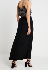 Svart maxikjol med en flödande siluett, kombinerad med en svart och vit crop top med blommönster. Har en bälte i midjan och blockklacksandaler.