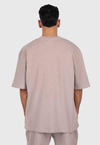 Chemise rose clair texturée à manches courtes en tissu côtelé. Coupe douce et oversize avec un col rond et des épaules tombantes.