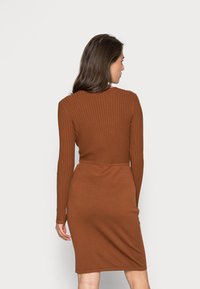 Vestido castanho de manga longa com textura canelada, apresentando uma silhueta ajustada e comprimento intermédio, destacando um design sem emendas e textura suave.