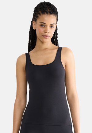 Woman with long braided hair wearing a fitted black sleeveless top, facing forward against a plain light background.