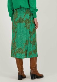 Jupe à imprimé floral vert avec une base marron, dotée d'une taille élastique et d'un design fluide. Portée avec des bottes marron jusqu'aux genoux.