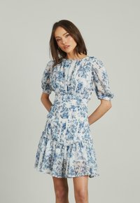 Abito floreale con maniche a sbuffo, caratterizzato da una gonna a strati in blu e bianco. Realizzato in tessuto leggero e trasparente con vita arricciata.