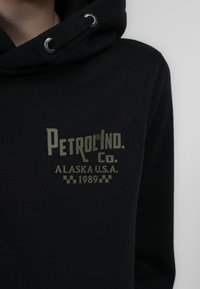 Felpa nera con cappuccio caratterizzata da un logo verde con la scritta "Petrol Ind. Co. Alaska U.S.A. 1989" e dettagli a scacchi nella parte bassa, in morbido cotone.