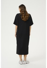 Black, knee-length dress with short sleeves. Made of soft fabric, features a relaxed fit and simple design. Paired with white and gray sneakers.