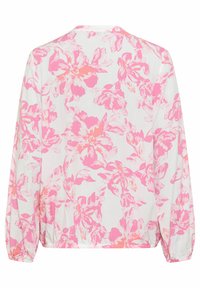 Blouse à manches longues avec un motif floral dans des tons de rose sur fond blanc. Dotée de poignets élastiques et d'une coupe décontractée.