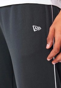 Graue Sporthosen mit weißen Seitenstreifen und einem kleinen gestickten Logo am Oberschenkel. Glatter Stoff mit bequemer Passform.