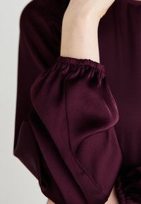 Burgundi-mekko, jossa on rynnäkkö, puffi hiha -design. Sileä kangas, ja elastiset hihansuut luovat kerätty�ä ilmettä ranteessa.