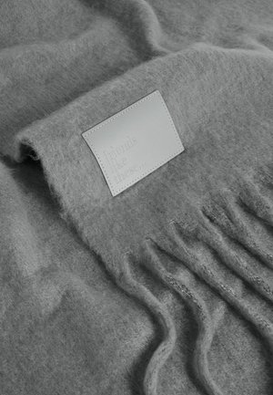 Écharpe en tricot grise fabriquée dans un matériau doux et texturé, présentant des bords à franges et une étiquette en cuir embossée avec "des amis comme ceux-là."