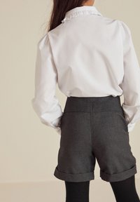 Cămașă albă cu guler volă, combinată cu pantaloni scurți gri închis cu talie înaltă, având mansete rulate și o textură fină.